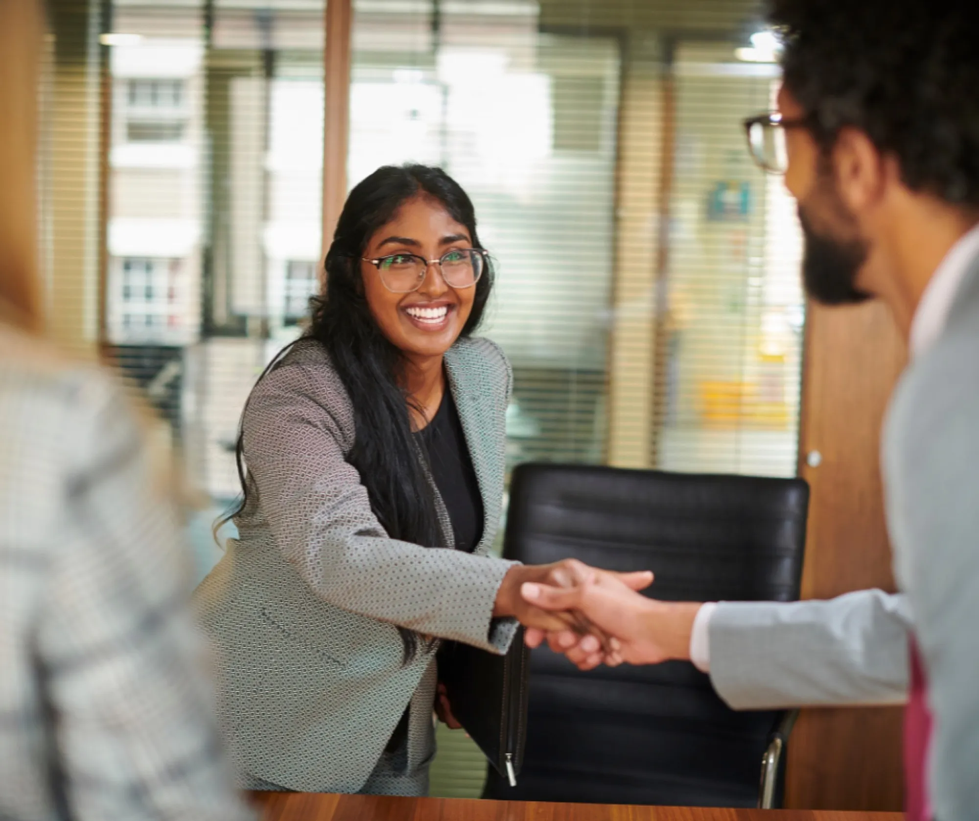 A smiling young professional shaking hands across a desk at an interview
